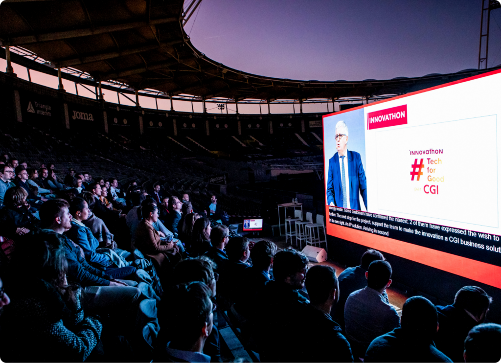 Vue panoramique de la tribune de la conférence, avec des participants assis et un grand écran